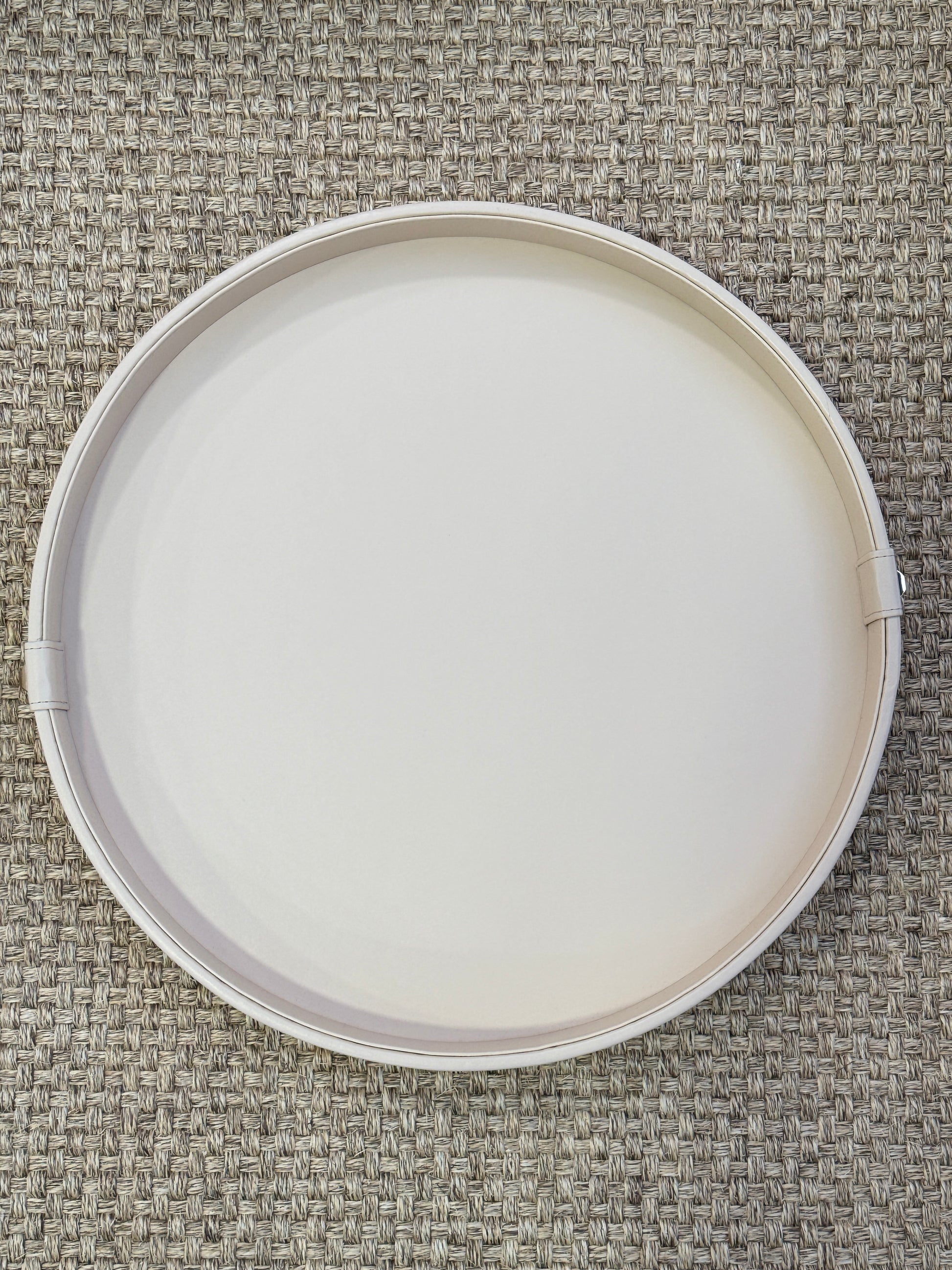 Detalle de bandeja redonda en polipiel beige con botón dorado, base de madera para mesa de centro