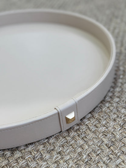 Vista superior de bandeja decorativa redonda en polipiel beige con botón dorado, diseño elegante y minimalista