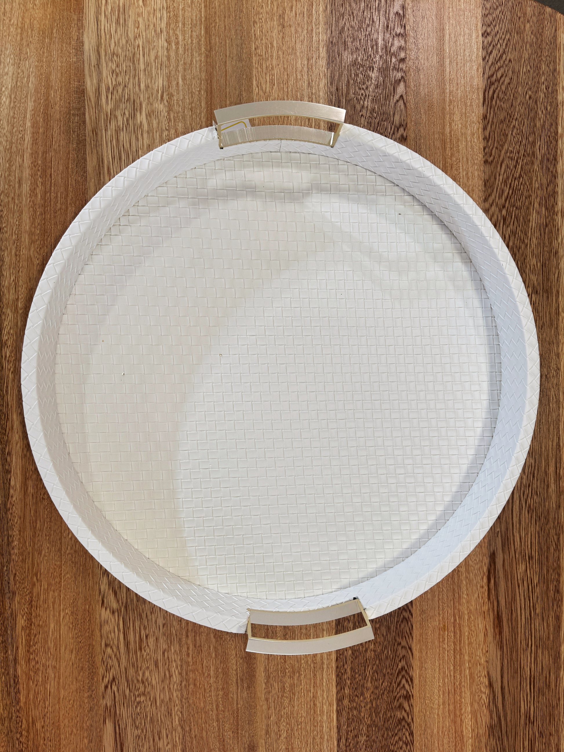 Vista superior de bandeja redonda en polipiel blanca con asas doradas de acero inoxidable, acabado premium