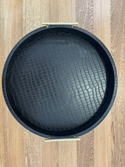 Detalle de bandeja redonda negra con asas doradas, base de madera revestida en polipiel para decoración