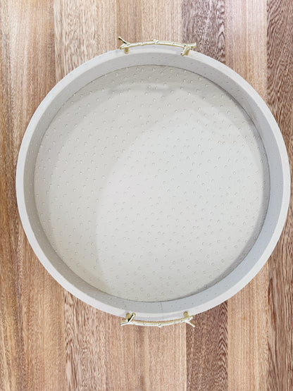 Vista superior de bandeja redonda en polipiel taupe con asas doradas de acero inoxidable, acabado premium