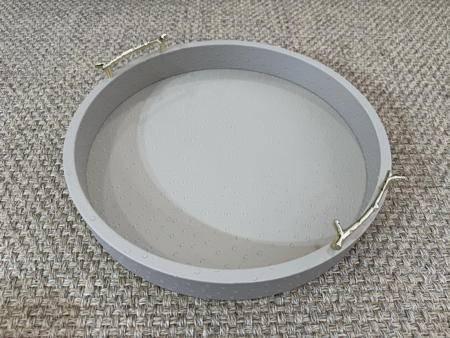 Detalle de bandeja redonda taupe con asas doradas, base de madera revestida en polipiel para decoración
