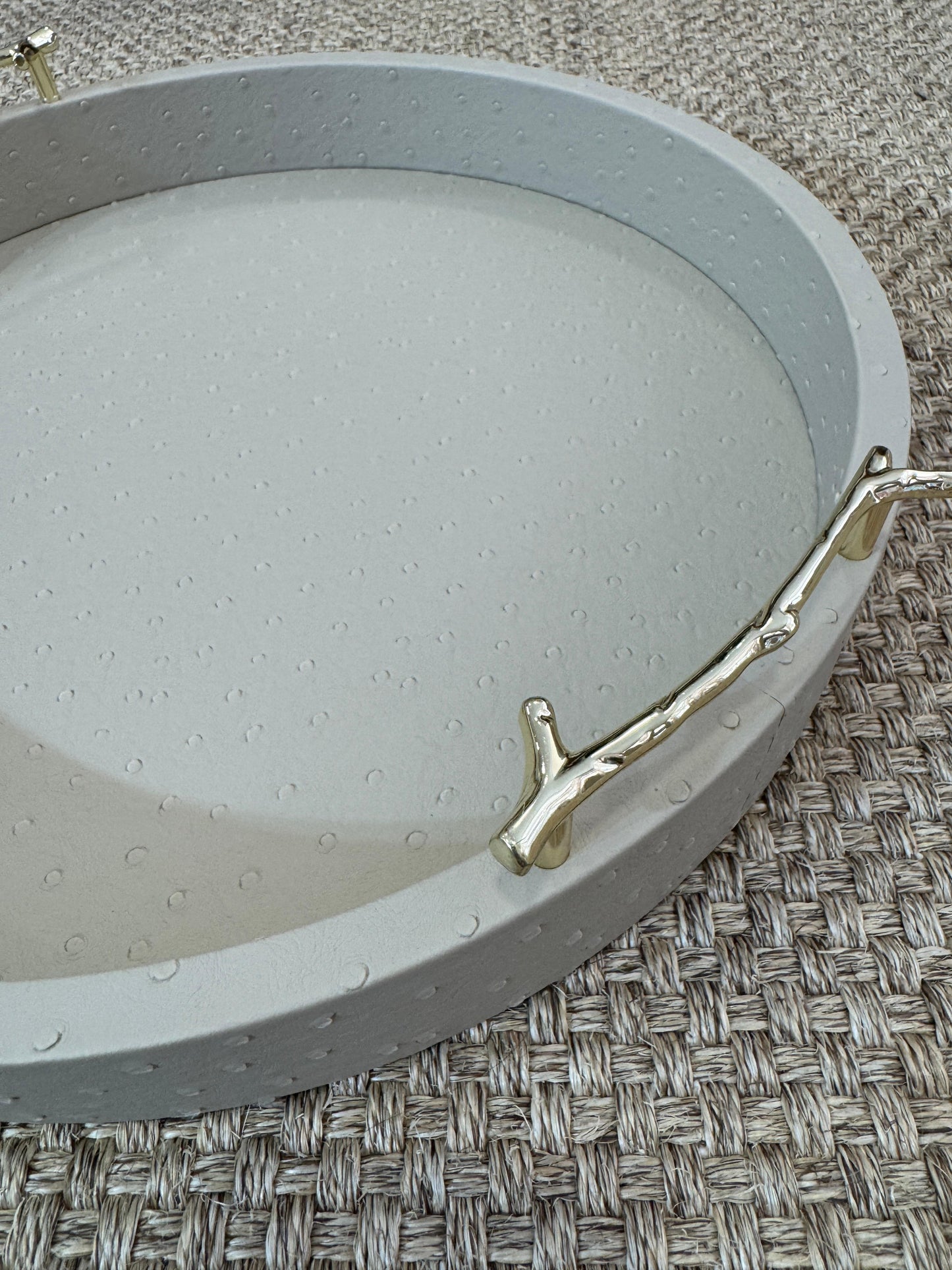 Bandeja decorativa redonda en polipiel taupe con asas metálicas doradas, estilo moderno y sofisticado