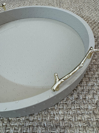 Bandeja decorativa redonda en polipiel taupe con asas metálicas doradas, estilo moderno y sofisticado