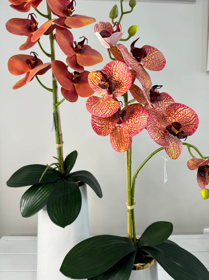 Detalle de jarrones de cerámica brillante con detalles dorados y orquídeas granate, arreglo decorativo para sala